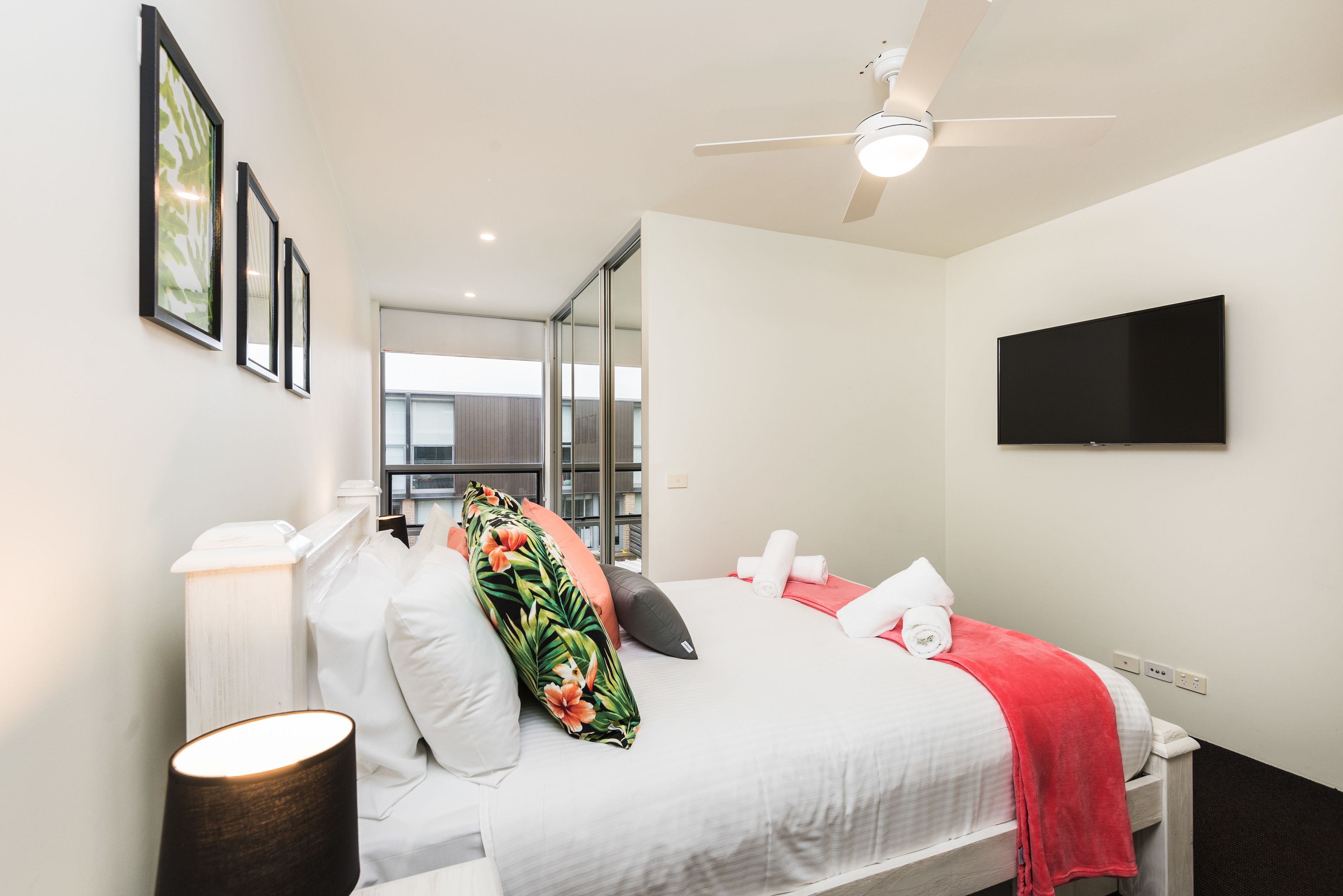 A modern hotel room with a bed, a flat-screen TV, and a ceiling fan.