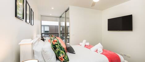 A modern hotel room with a bed, a flat-screen TV, and a ceiling fan.
