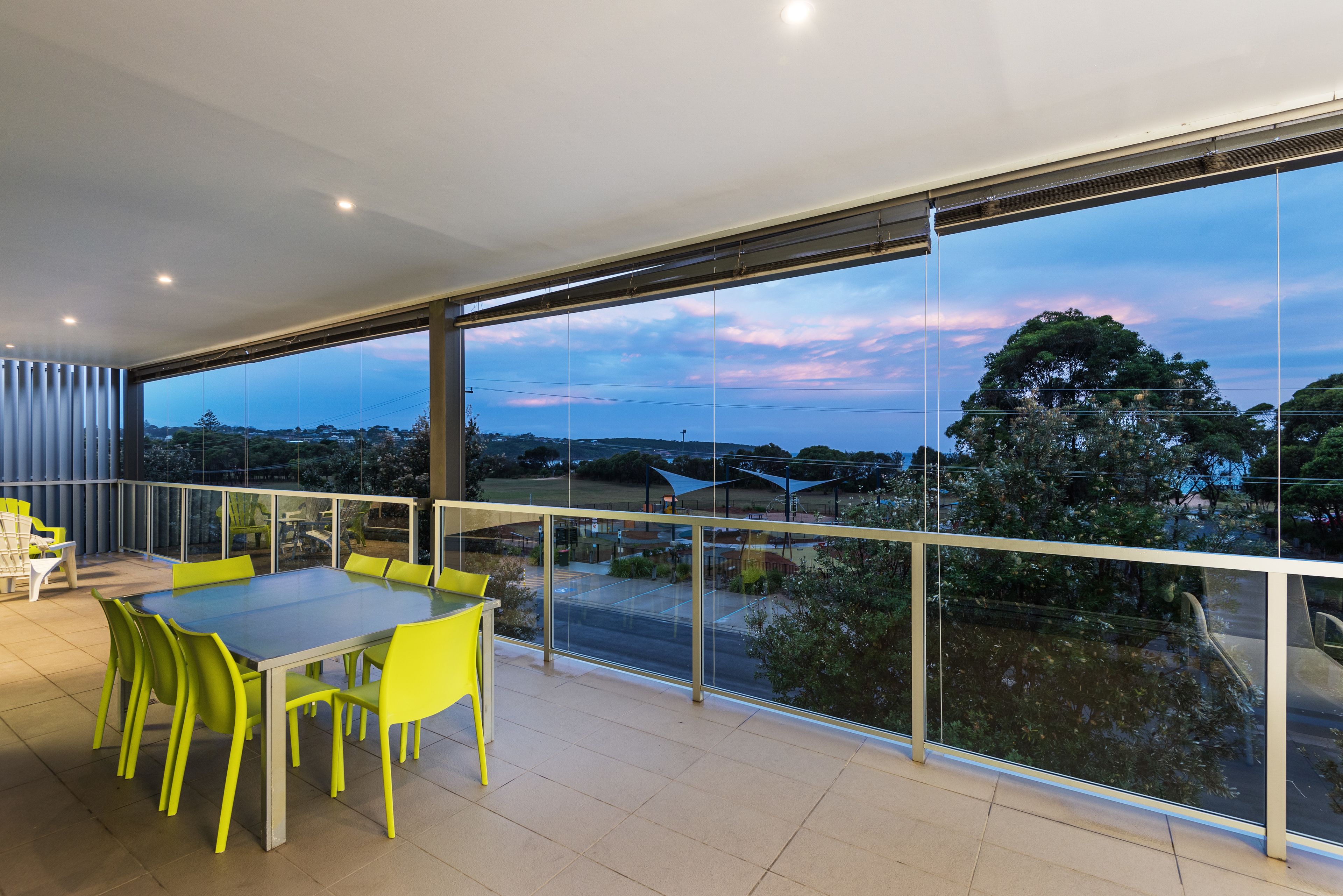 A balcony with a glass railing, a table with chairs, and a view of the landscape.