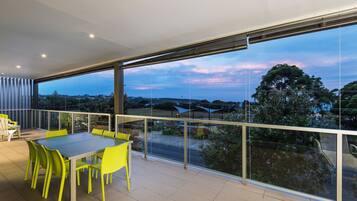 A balcony with a glass railing, a table with chairs, and a view of the landscape.
