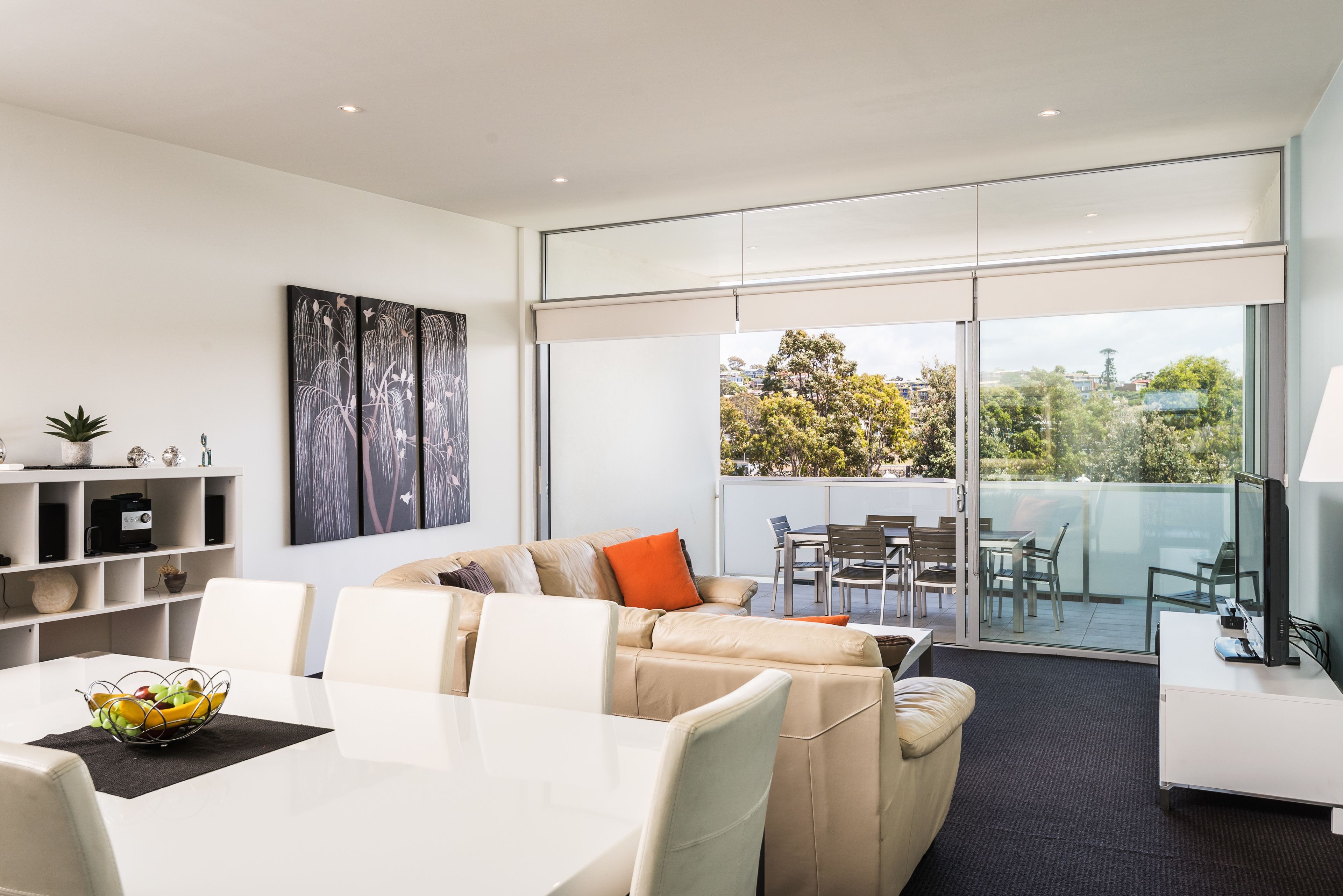 A modern living room with a sofa, dining table, and a balcony with outdoor furniture.