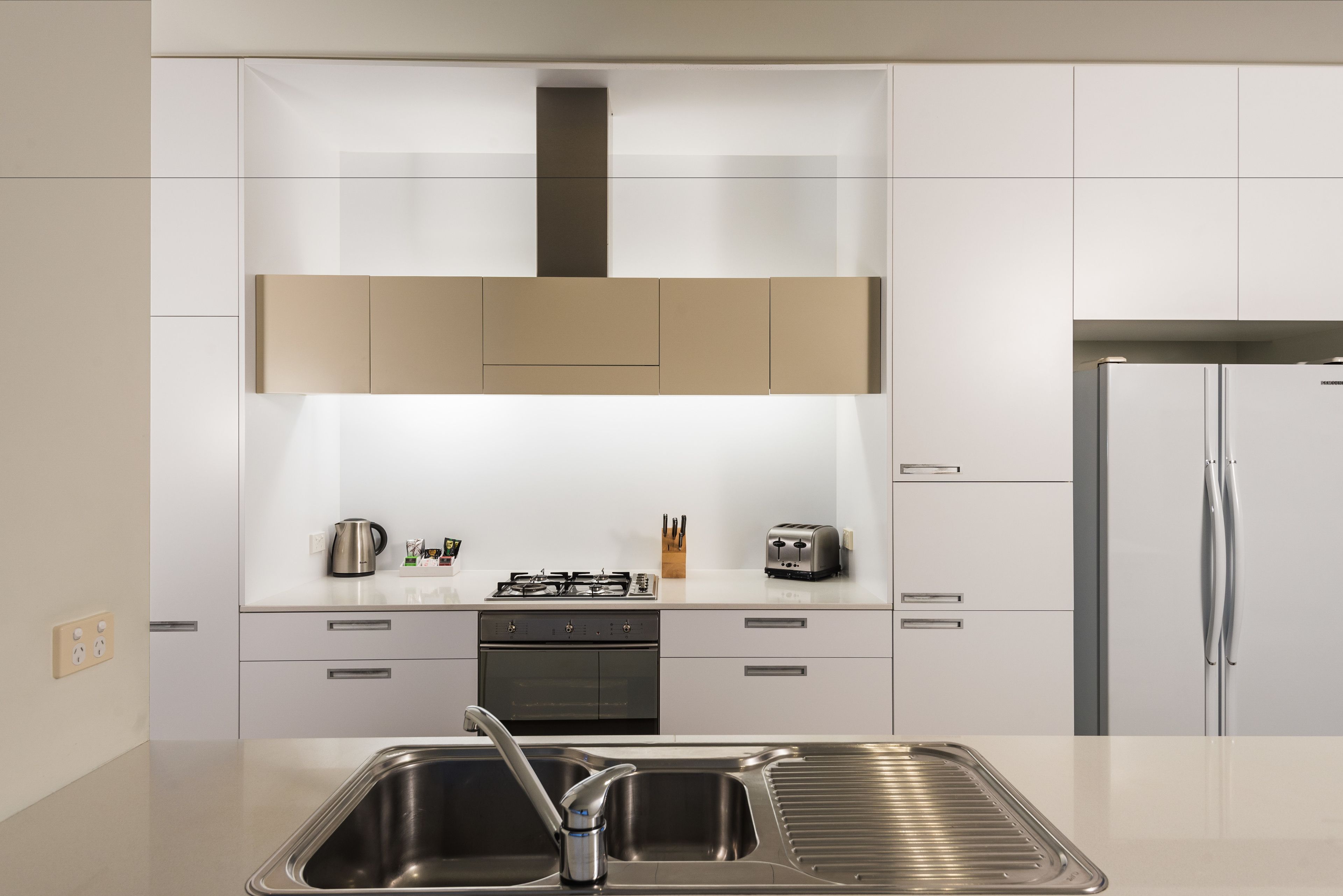 Eine moderne Küche mit weißen Schränken, einer Edelstahl-Spüle, einem Gasherd und einem Kühlschrank.