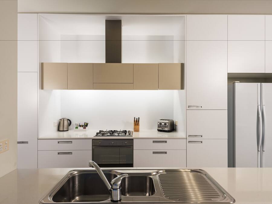 Eine moderne Küche mit weißen Schränken, einer Edelstahl-Spüle, einem Gasherd und einem Kühlschrank.