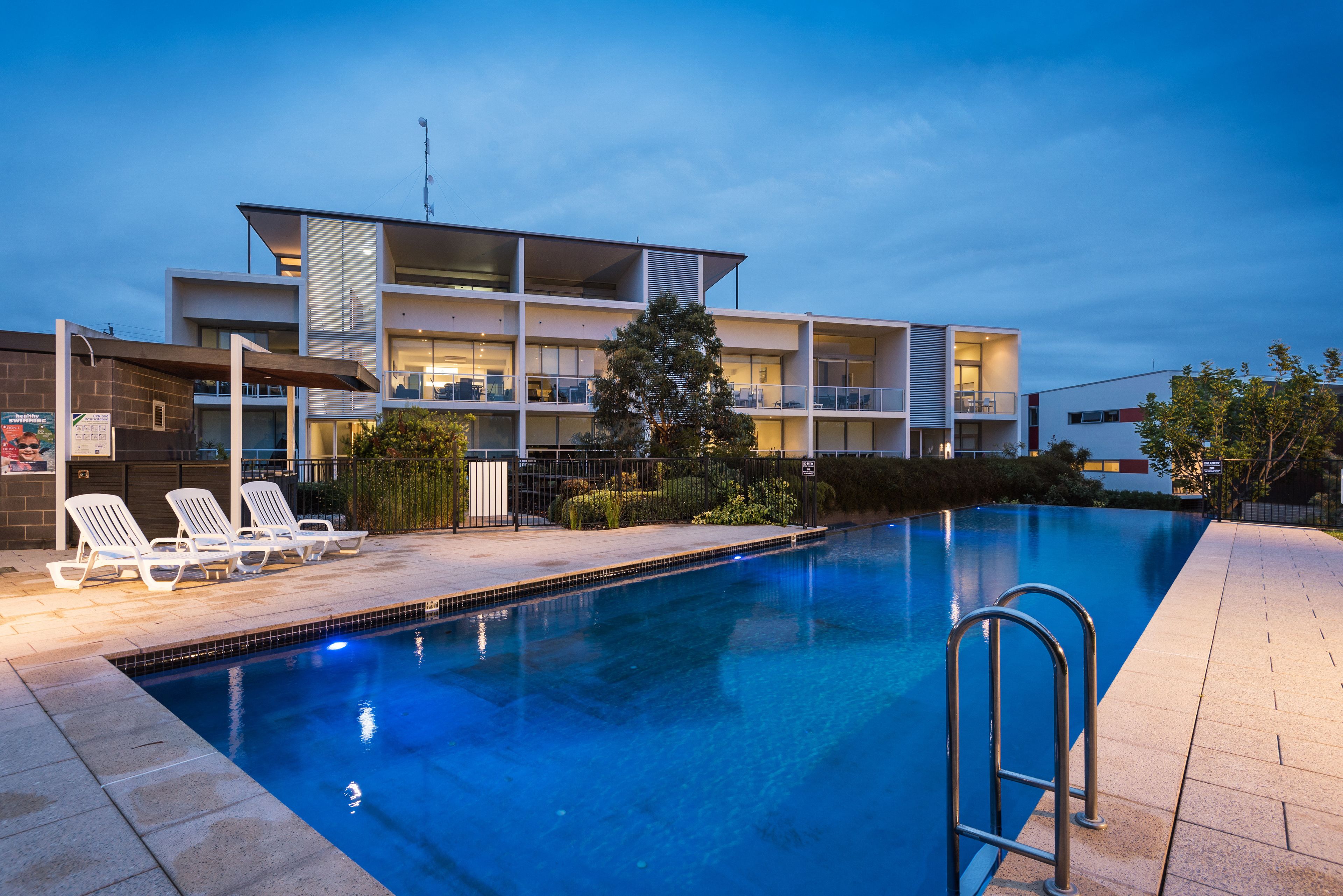 A modern hotel with a swimming pool, lounge chairs, and a well-lit outdoor area.
