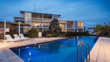 A modern hotel with a swimming pool, lounge chairs, and a well-lit outdoor area.