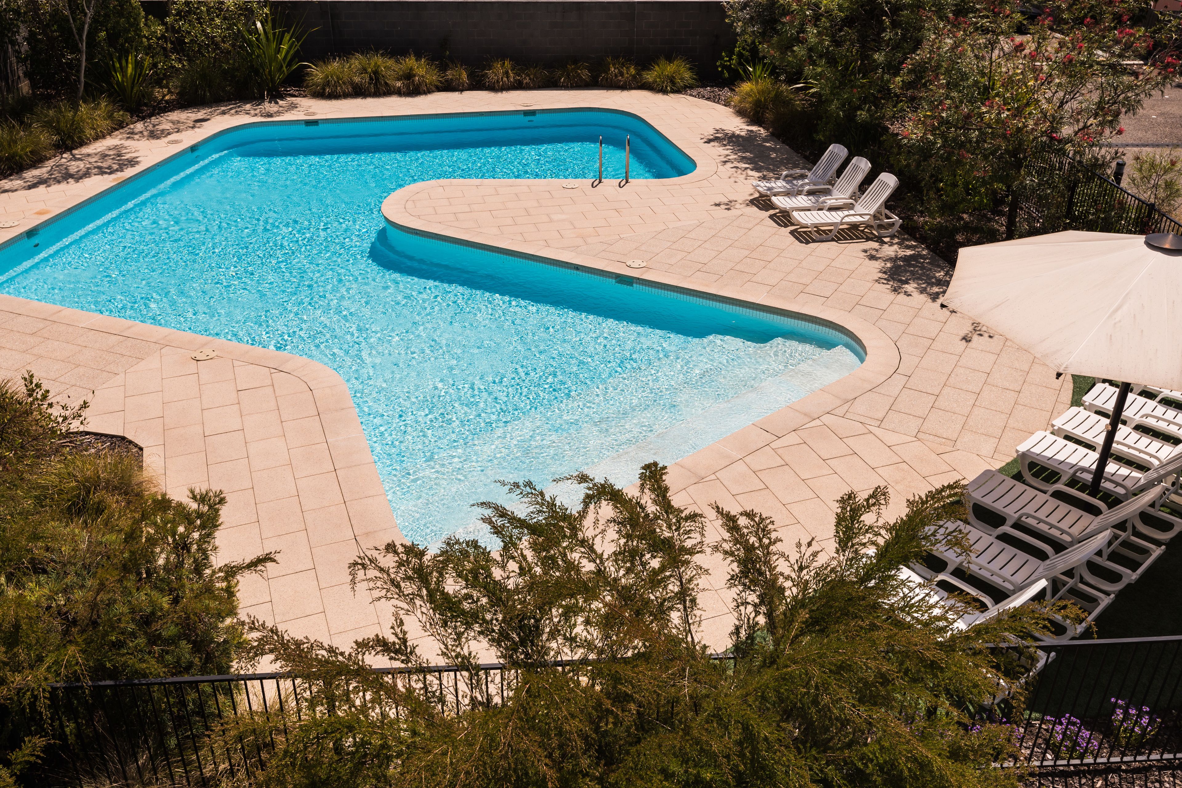 Piscina com design curvo, rodeada por um deck revestido de azulejos e espreguiçadeiras.