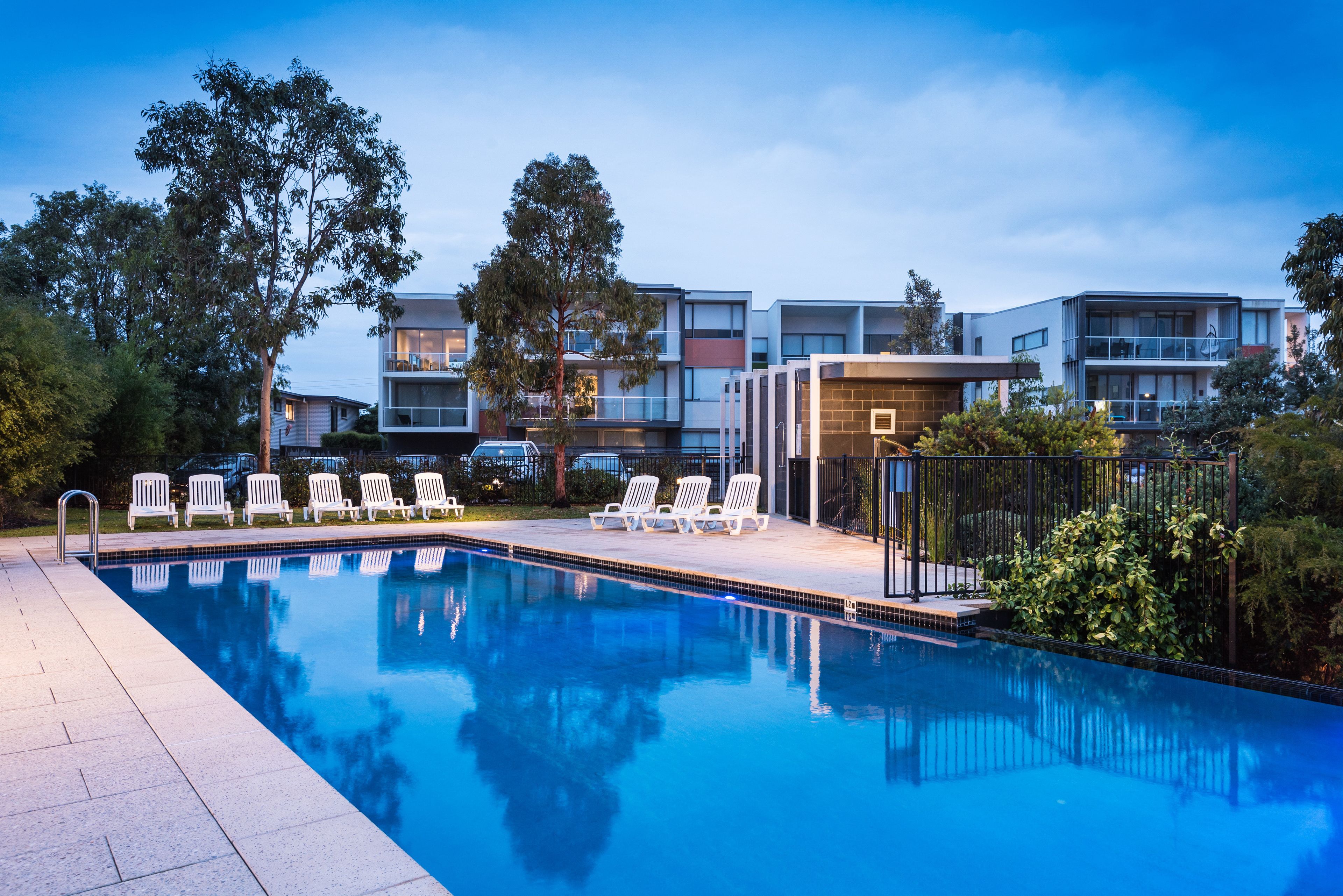 A swimming pool with lounge chairs and a building with multiple balconies in the background.