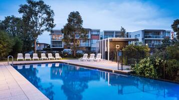A swimming pool with lounge chairs and a building with multiple balconies in the background.