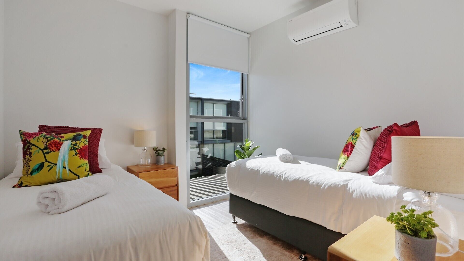 Une chambre d’hôtel moderne avec deux lits, une petite table, une lampe et une vue sur l’extérieur.