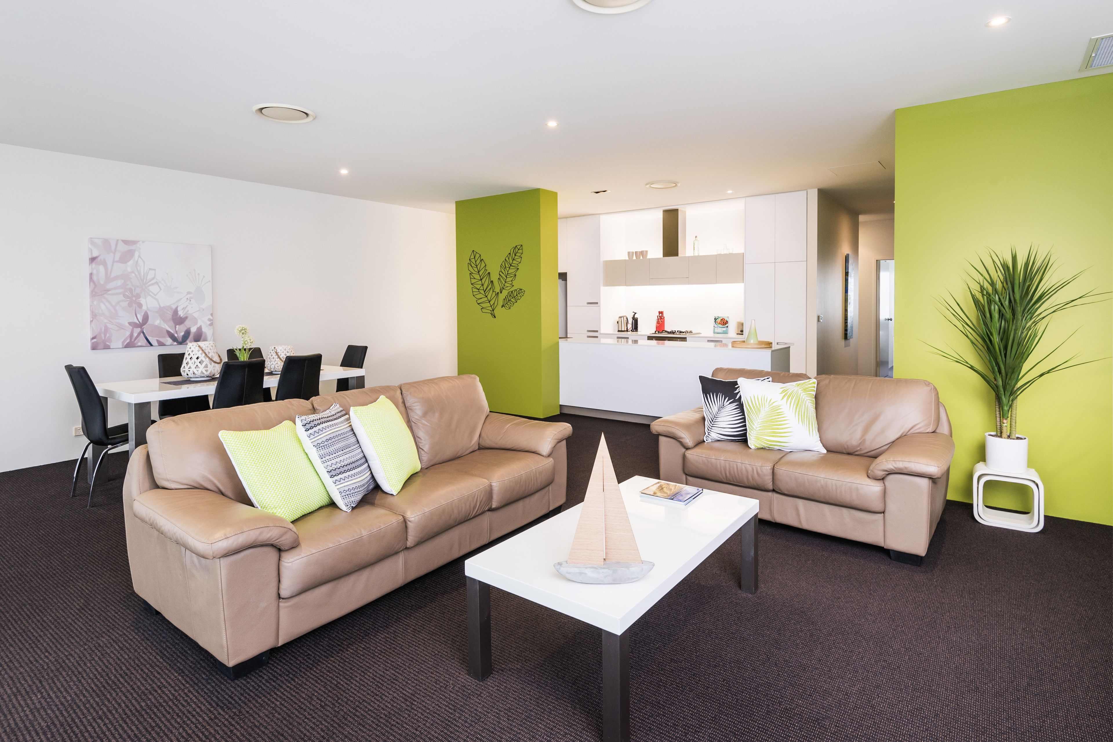 A modern living room with two leather sofas, a white coffee table, and a dining area with a white table and chairs.