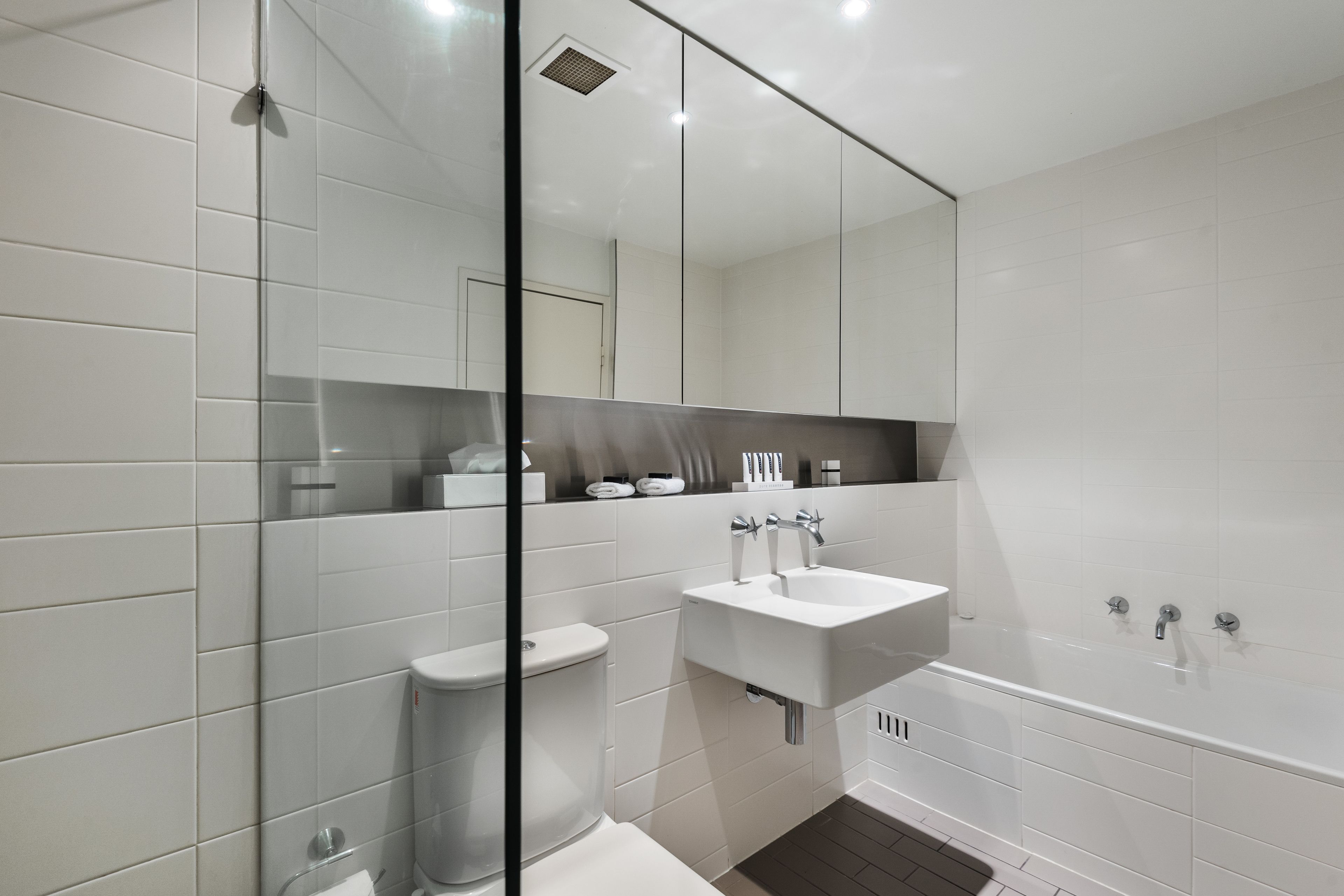 A modern bathroom with white tiles, a glass shower enclosure, a white sink, and a bathtub.