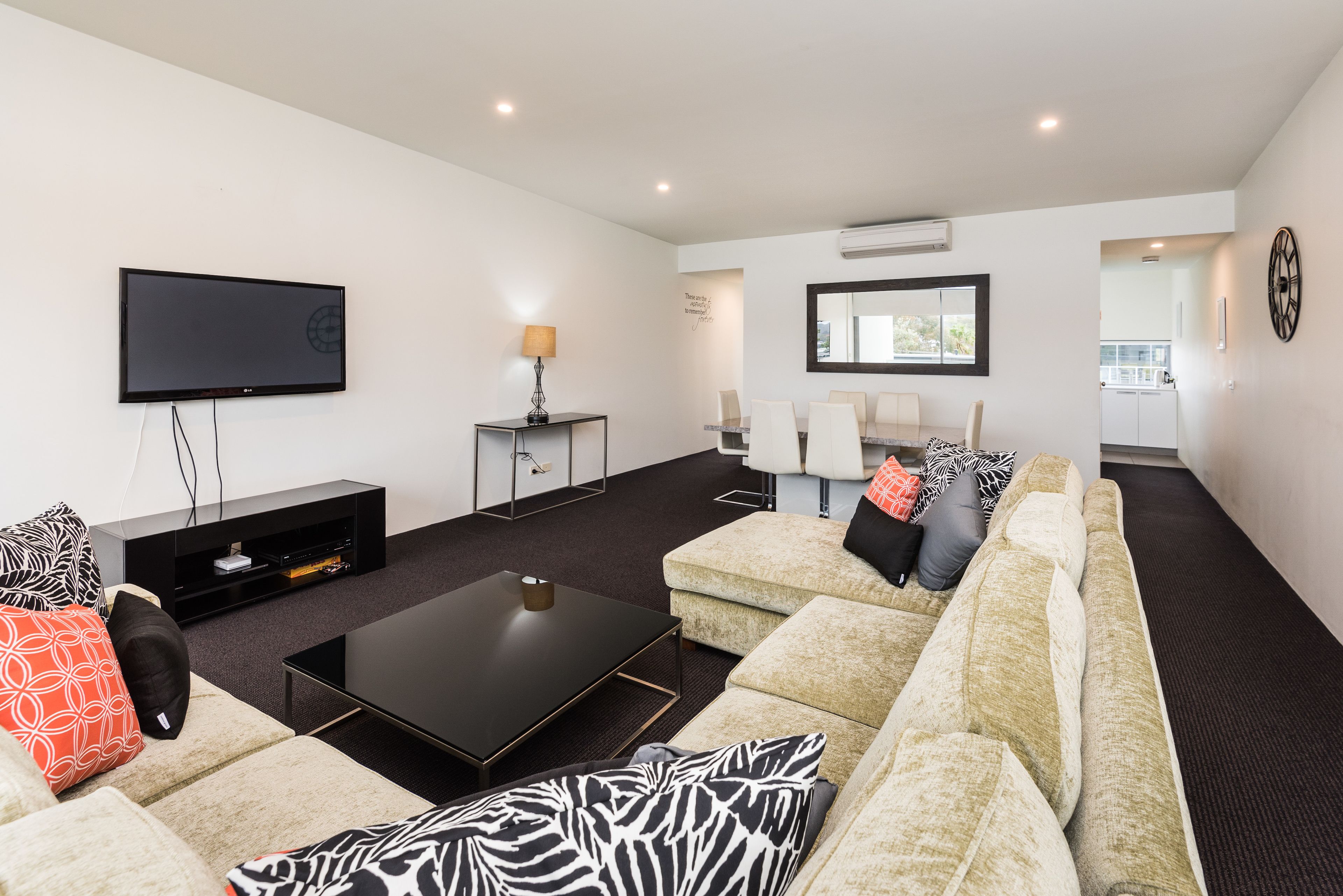 Una sala de estar moderna con televisor de pantalla plana, una mesa de centro, un conjunto de sofás y un comedor con sillas y una mesa.