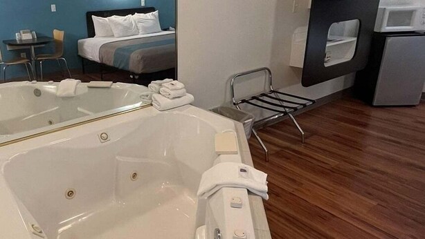 Et hotelværelse med et stort badekar, en seng, et skrivebord og et spejl.