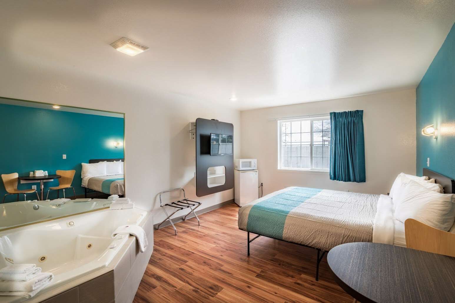 A modern hotel room with a bed, a sitting area, a small table, a microwave, and a window with curtains.