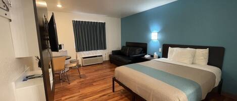 A hotel room with a bed, a desk, a chair, a TV, and a window with curtains.