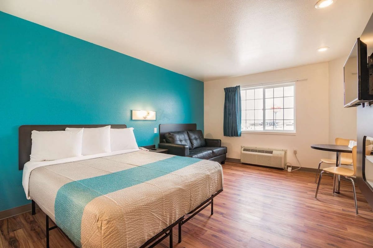A hotel room with a bed, a desk, a chair, a TV, and a window with curtains.