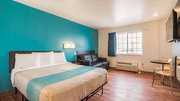 A hotel room with a bed, a desk, a chair, a TV, and a window with curtains.