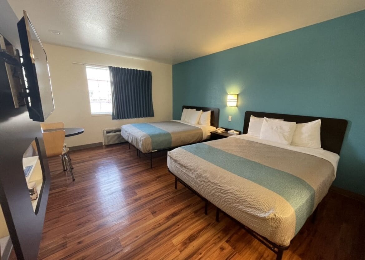 A hotel room with two beds, a desk, and a TV.
