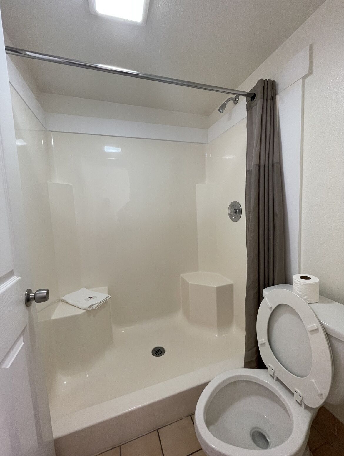 A modern bathroom with a walk-in shower, toilet, and a small storage shelf.