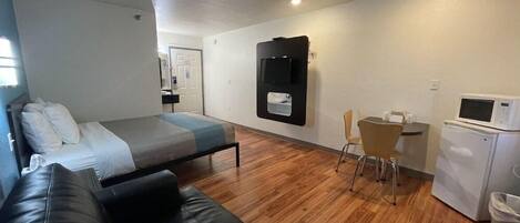 A compact room with a bed, a black leather couch, a small desk with a chair, a microwave, and a refrigerator.