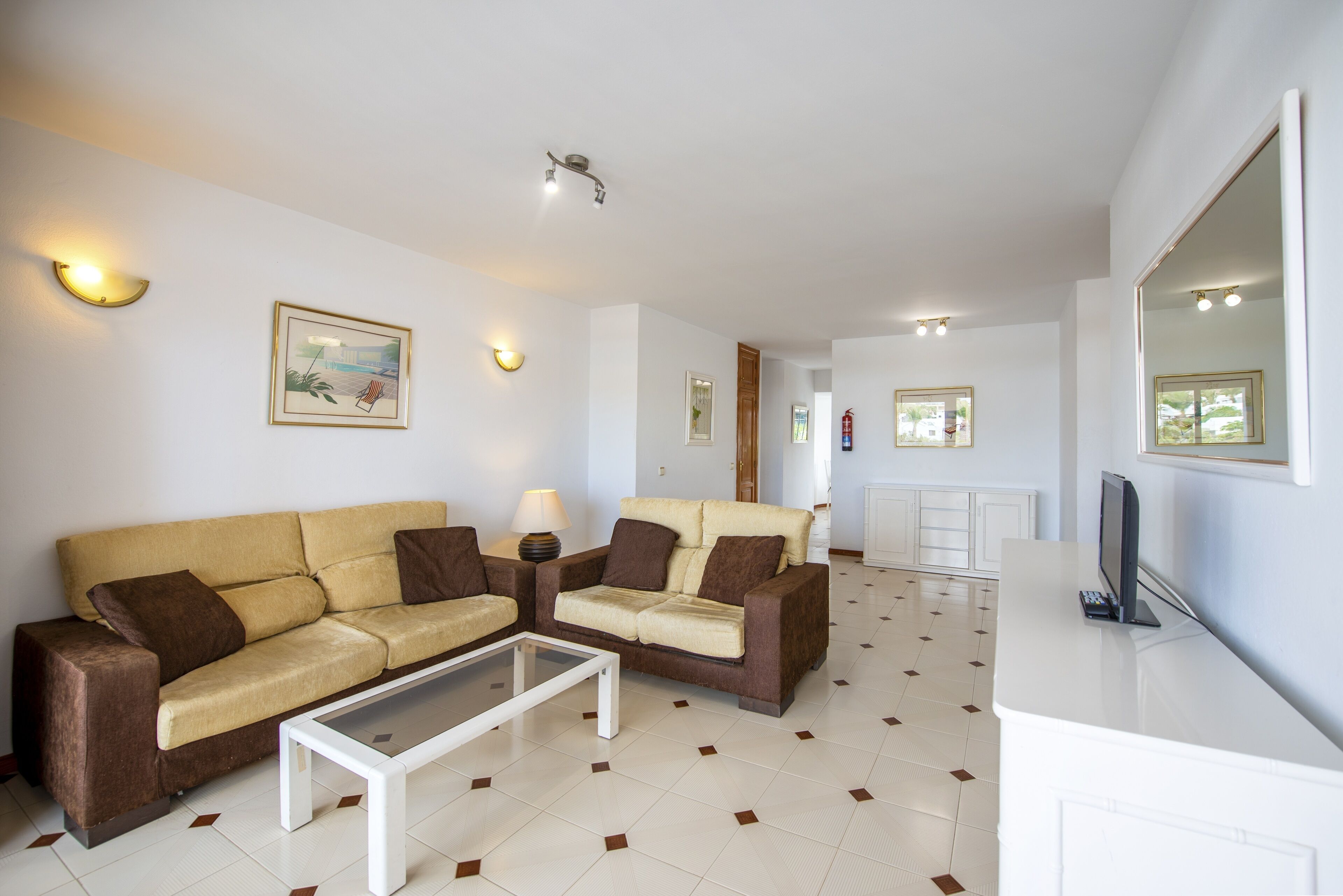 Una sala de estar con dos sofás, una mesa de centro y un televisor sobre un mueble blanco.