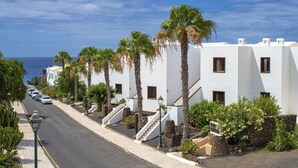 Una calle costera bordeada por edificios blancos, palmeras y una vista despejada del mar.