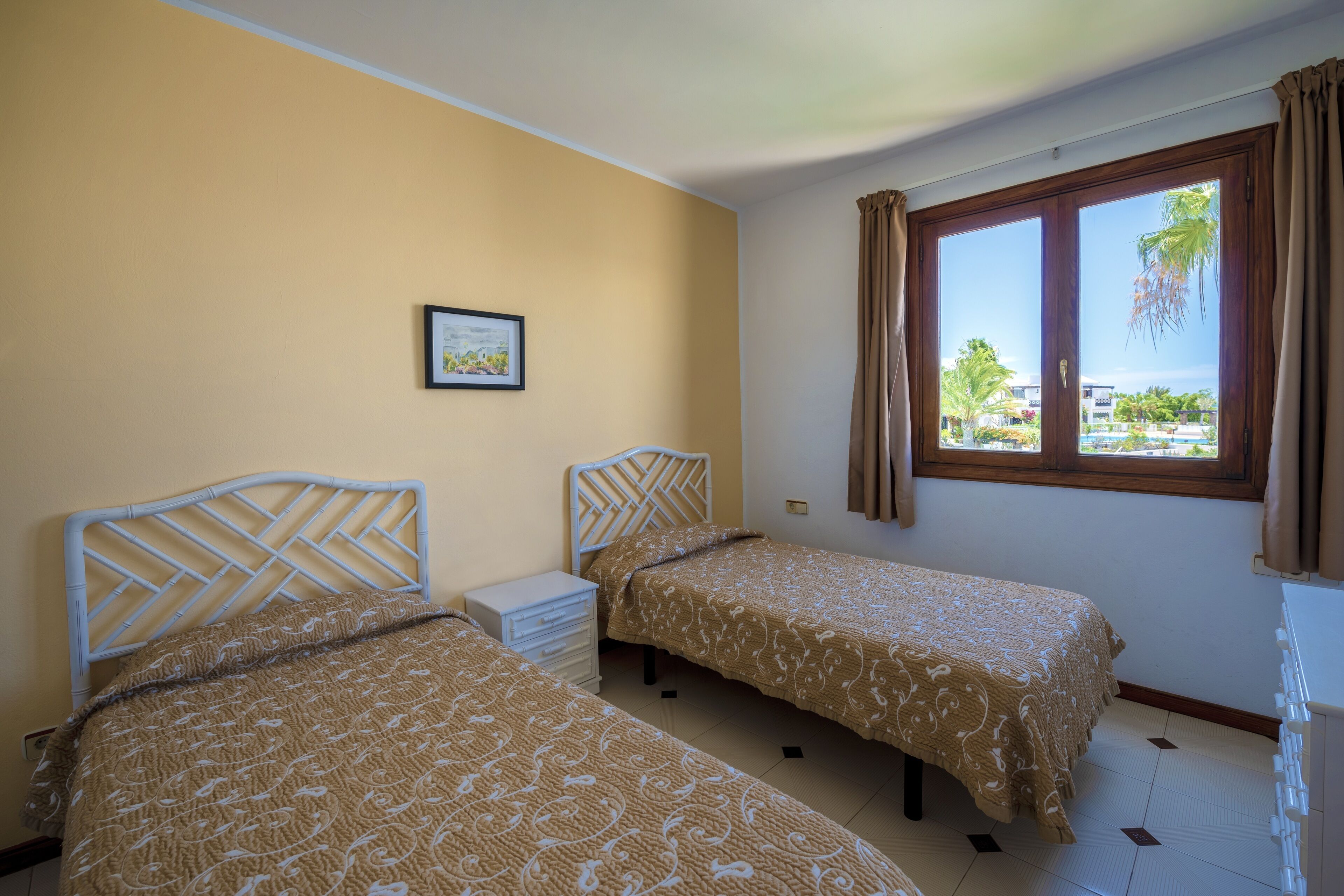 A room with two beds, a nightstand, a window with curtains, and a framed picture on the wall.