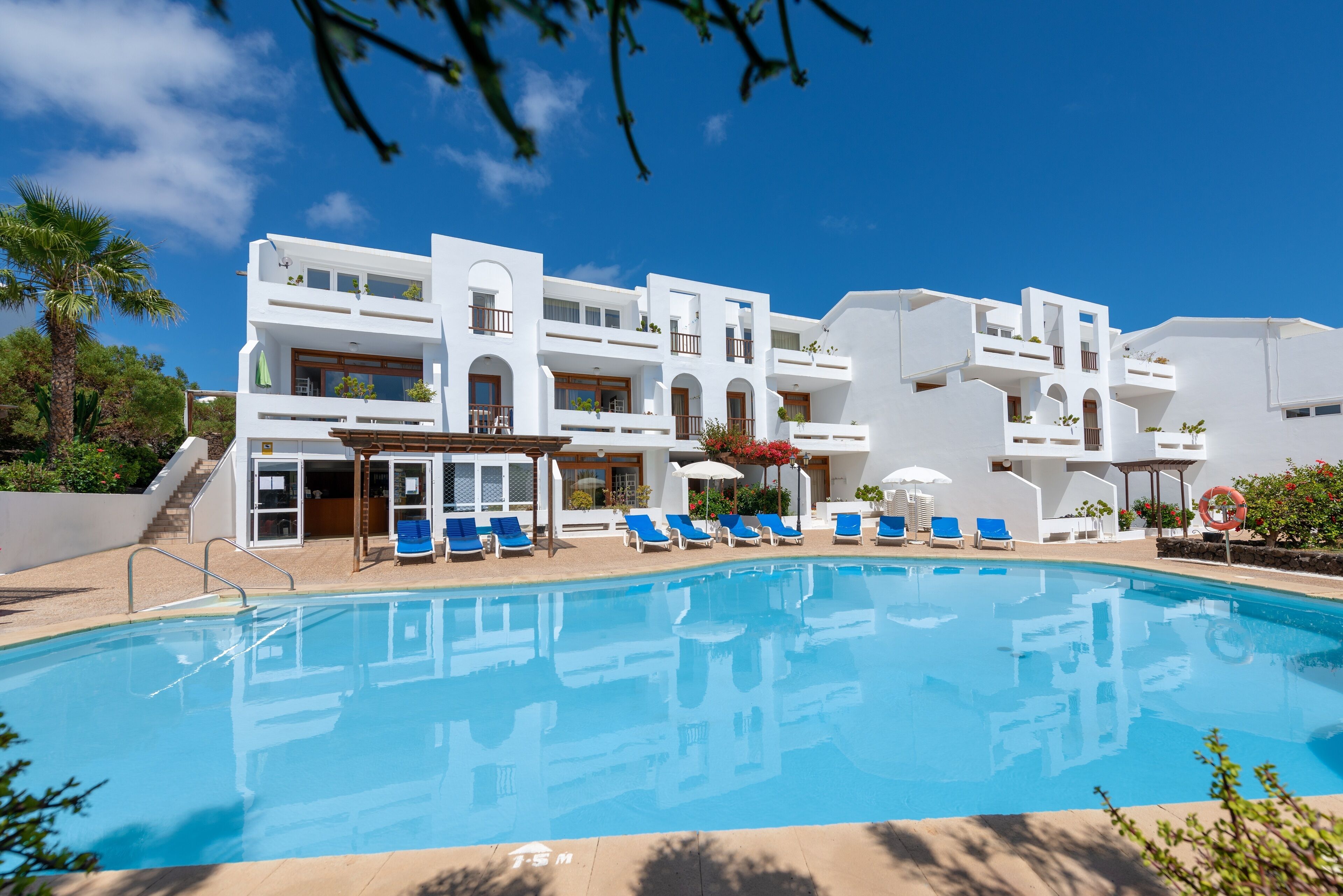 Un hotel moderno con piscina, sillones azules y fachada blanca.