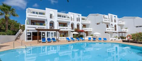 Un hotel moderno con piscina, sillones azules y fachada blanca.