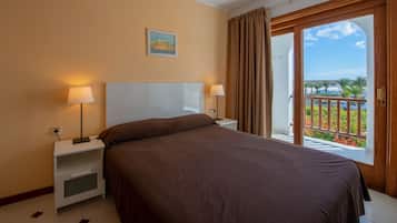 A hotel room with a bed, two bedside tables with lamps, a painting on the wall, and a balcony with a view.