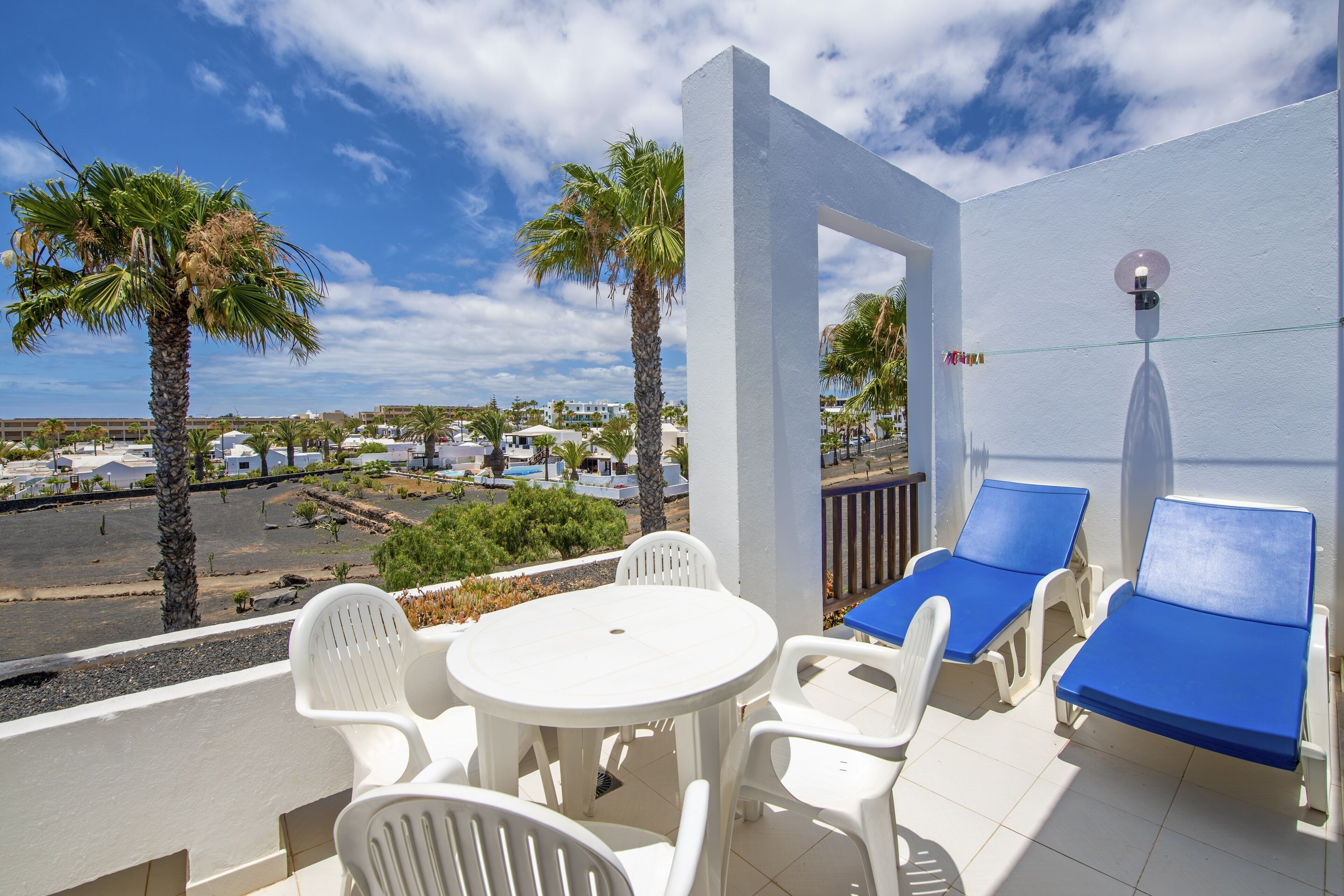 A balcony with white chairs, a round table, and blue sun loungers.