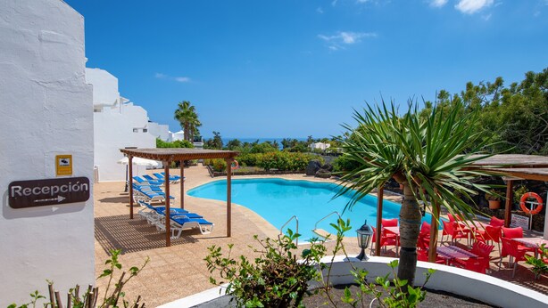 Zona de piscina con sillones de descanso, un letrero de recepción y vista despejada al mar.