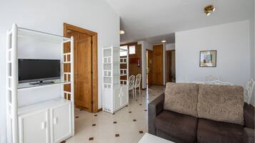 Un salon avec un téléviseur posé sur une étagère en verre, un canapé et un coin repas avec des chaises.