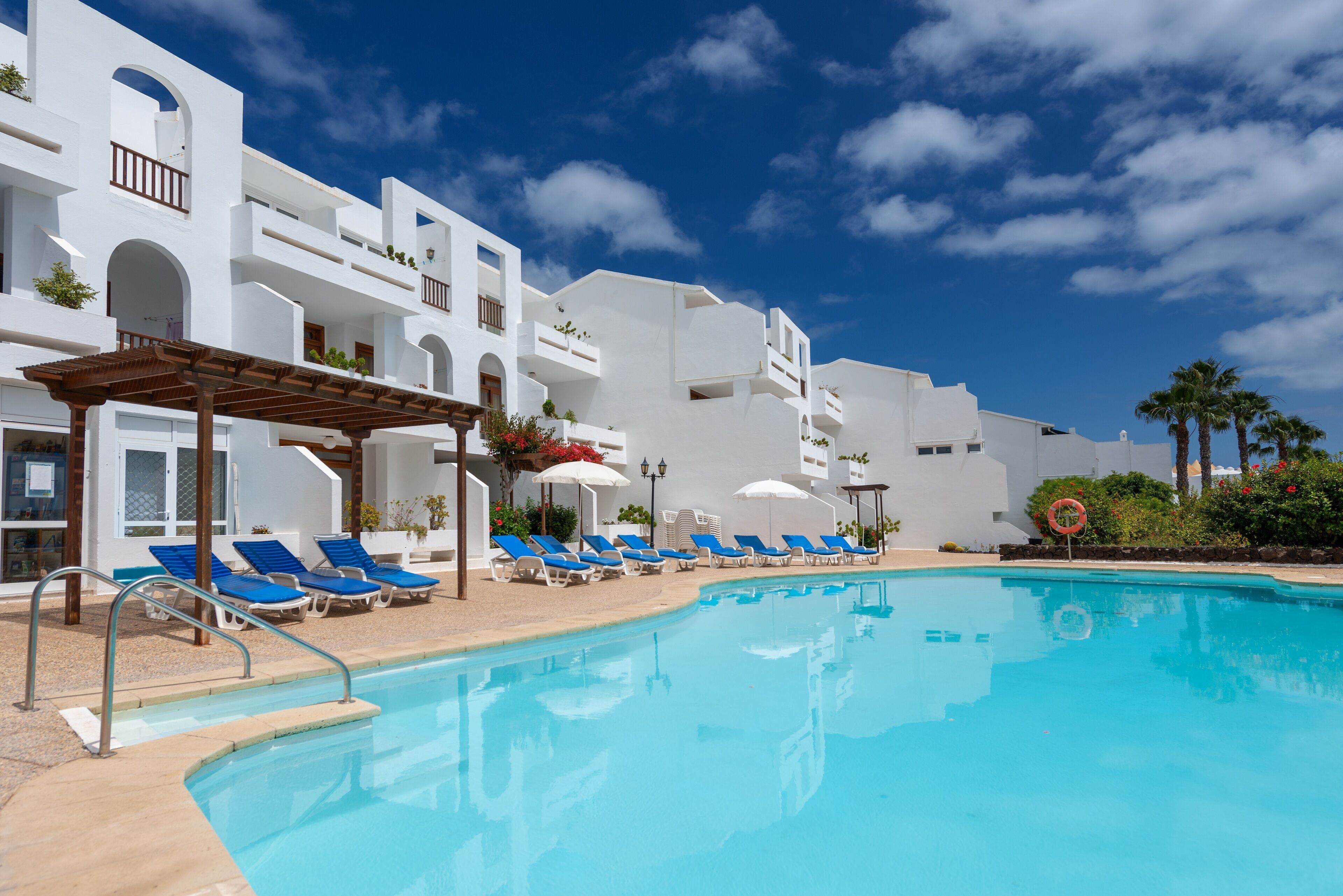 A pool area with blue lounge chairs and white buildings with balconies.