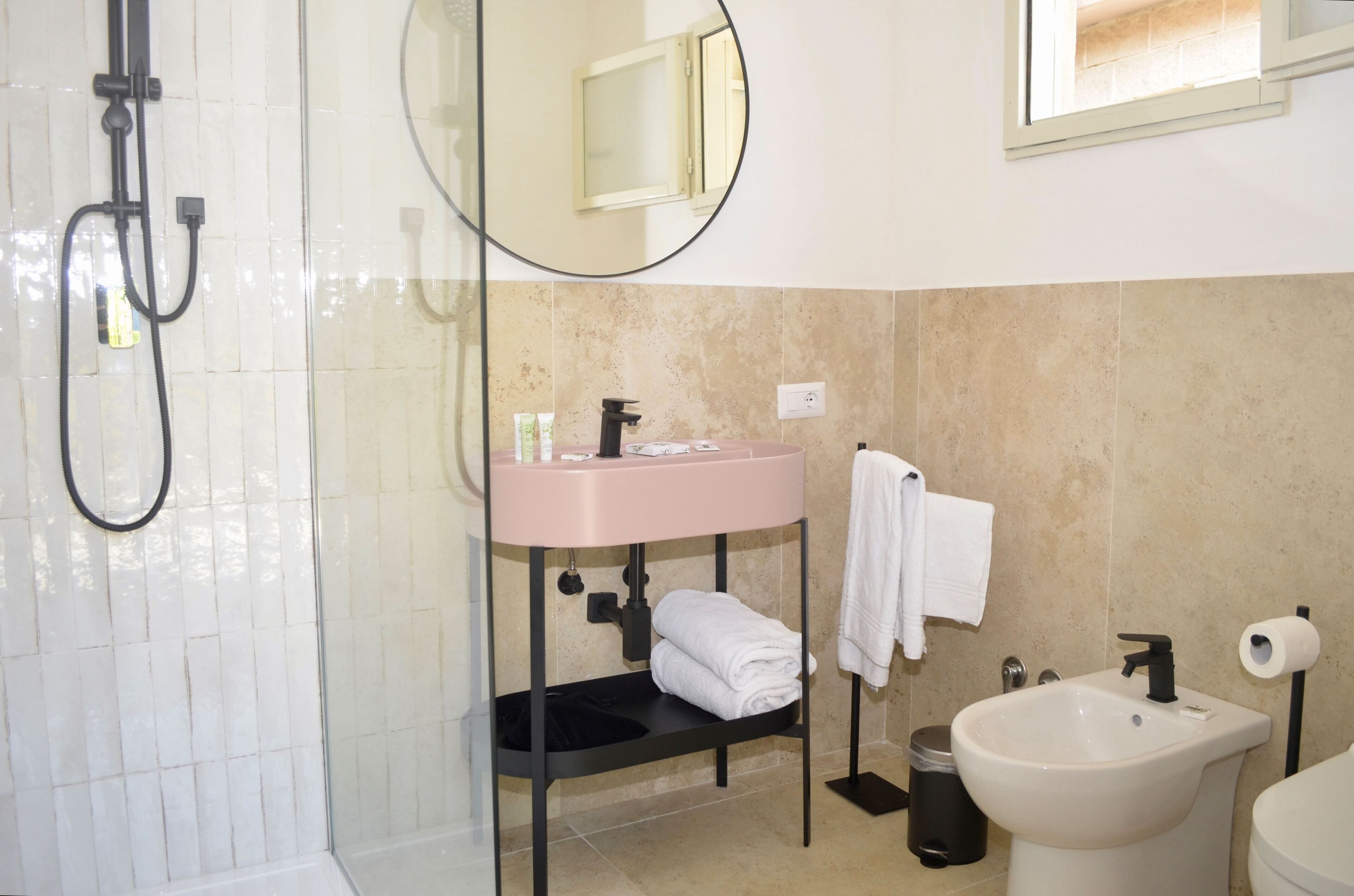 Ein Badezimmer mit einer Duschkabine, einem rosa Waschbecken, einem Spiegel, einem Handtuchhalter und einem Bidet.