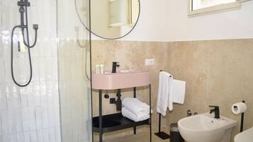 Une salle de bain avec une douche à parois de verre, un lavabo rose, un miroir, un porte-serviettes et un bidet.