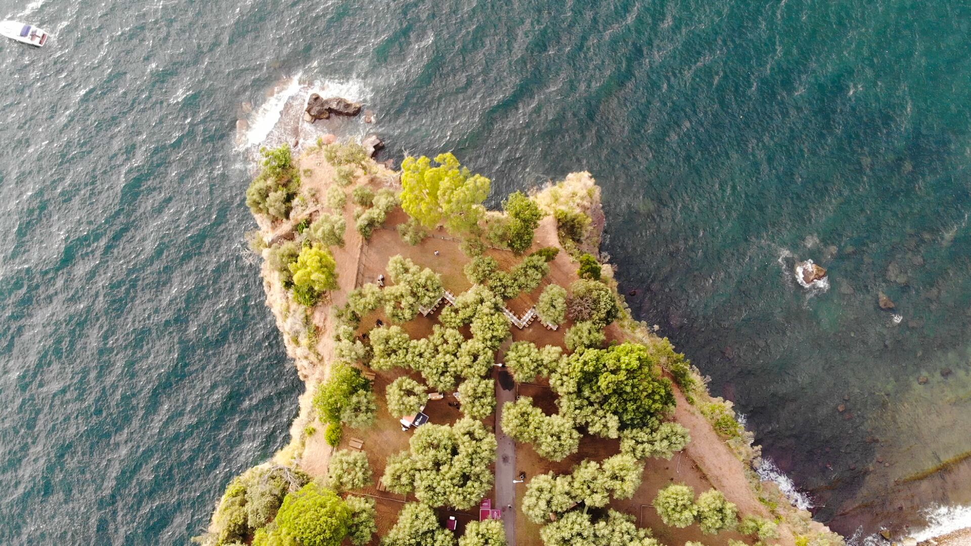 An aerial view of a coastal area with a small settlement, including a paved path and scattered buildings.