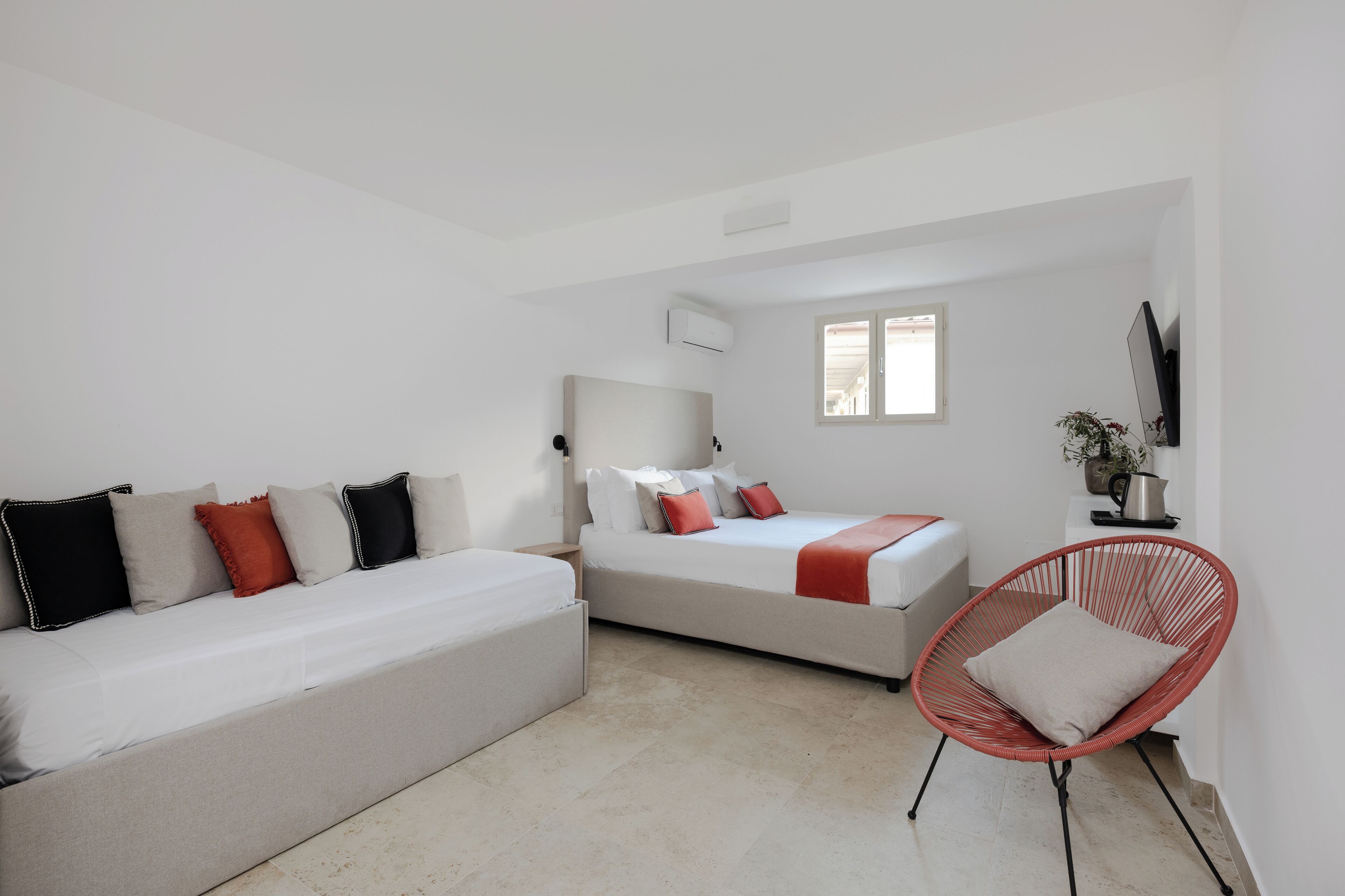 Une chambre à coucher moderne et minimaliste, avec un canapé, un lit, un fauteuil rouge et un téléviseur.