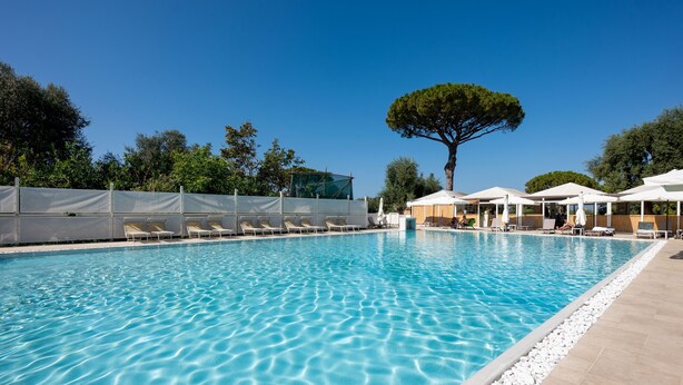 A clear blue swimming pool with lounge chairs and umbrellas, surrounded by trees and a clear sky. - Sopramare Resort (Piano di Sorrento)