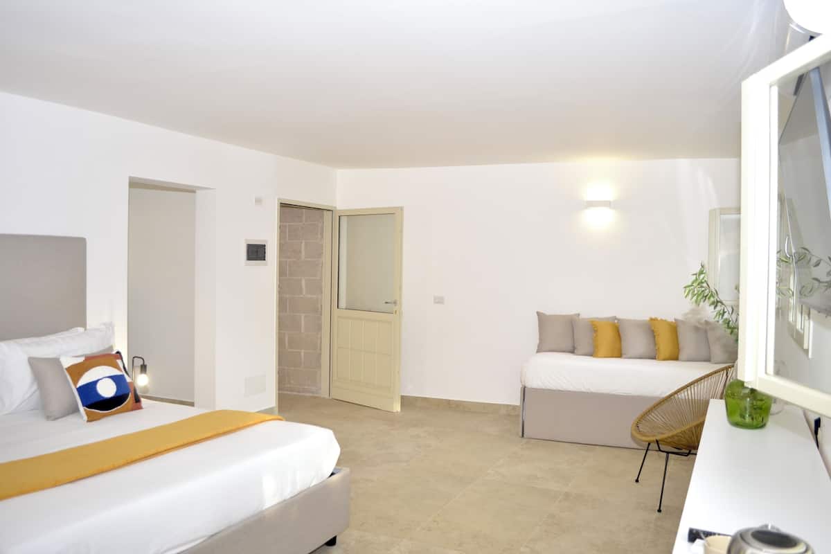 A modern hotel room with a bed, a sofa, a chair, and a desk.