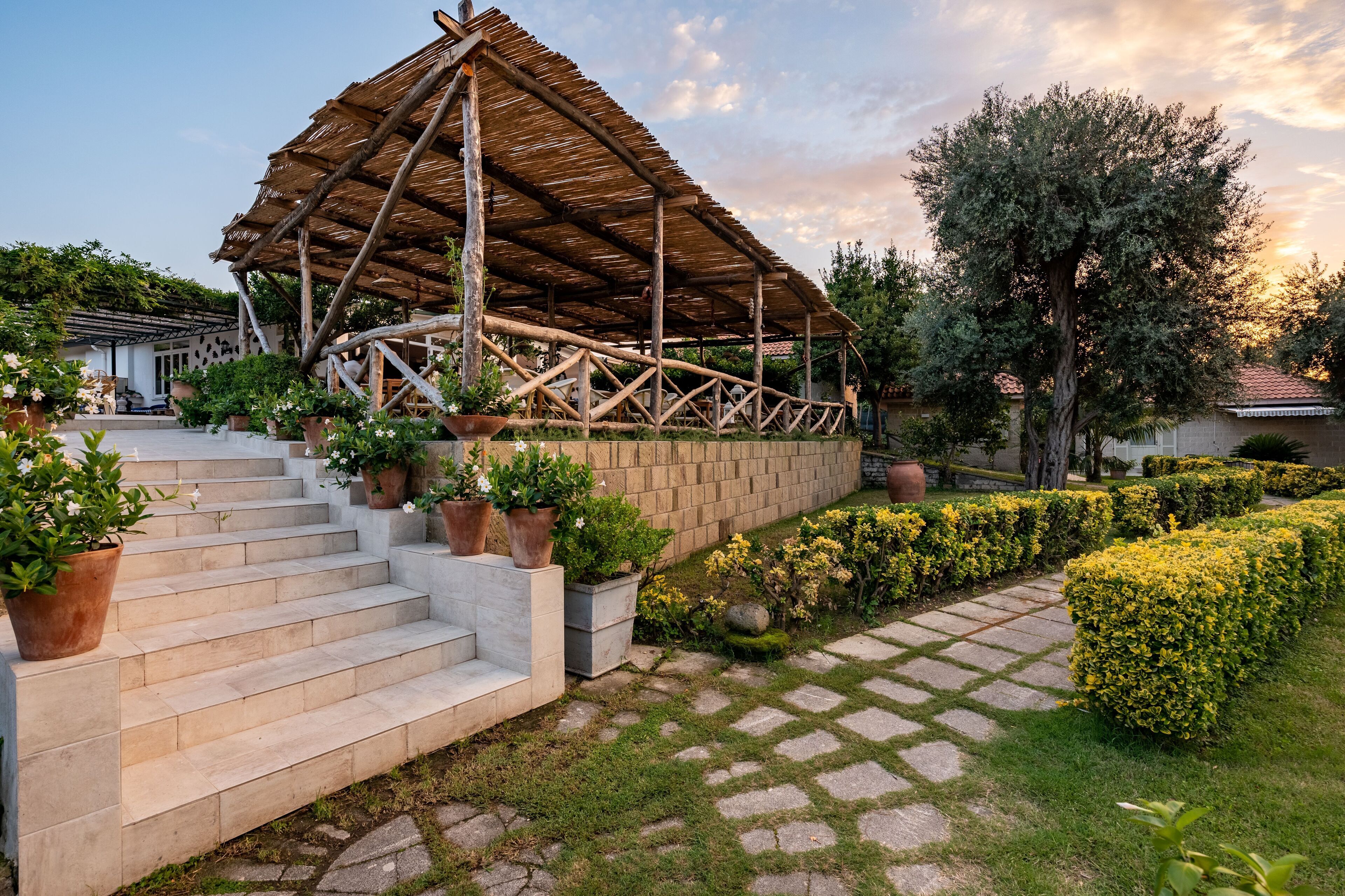 A covered outdoor area with steps leading to a building, surrounded by potted plants and a well-maintained garden.