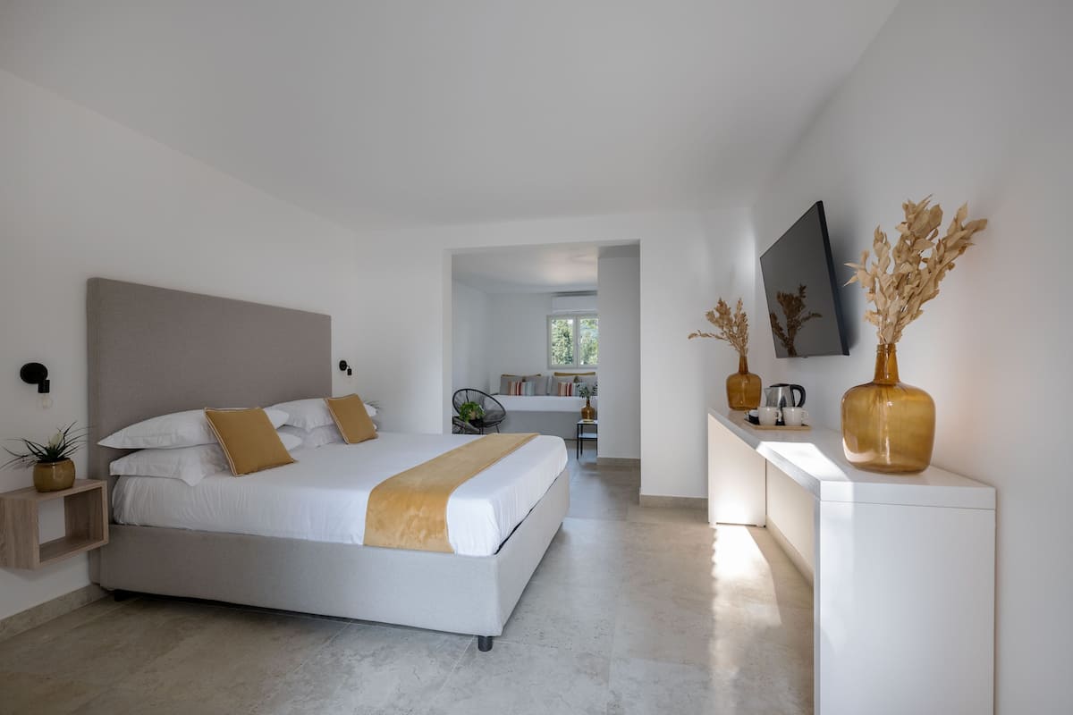A modern bedroom with a large bed, bedside tables, a small desk, and a TV mounted on the wall.