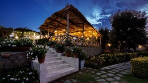 A rustic wooden structure with a thatched roof, surrounded by a garden with potted plants and a stone pathway. - Sopramare Resort (Piano di Sorrento)