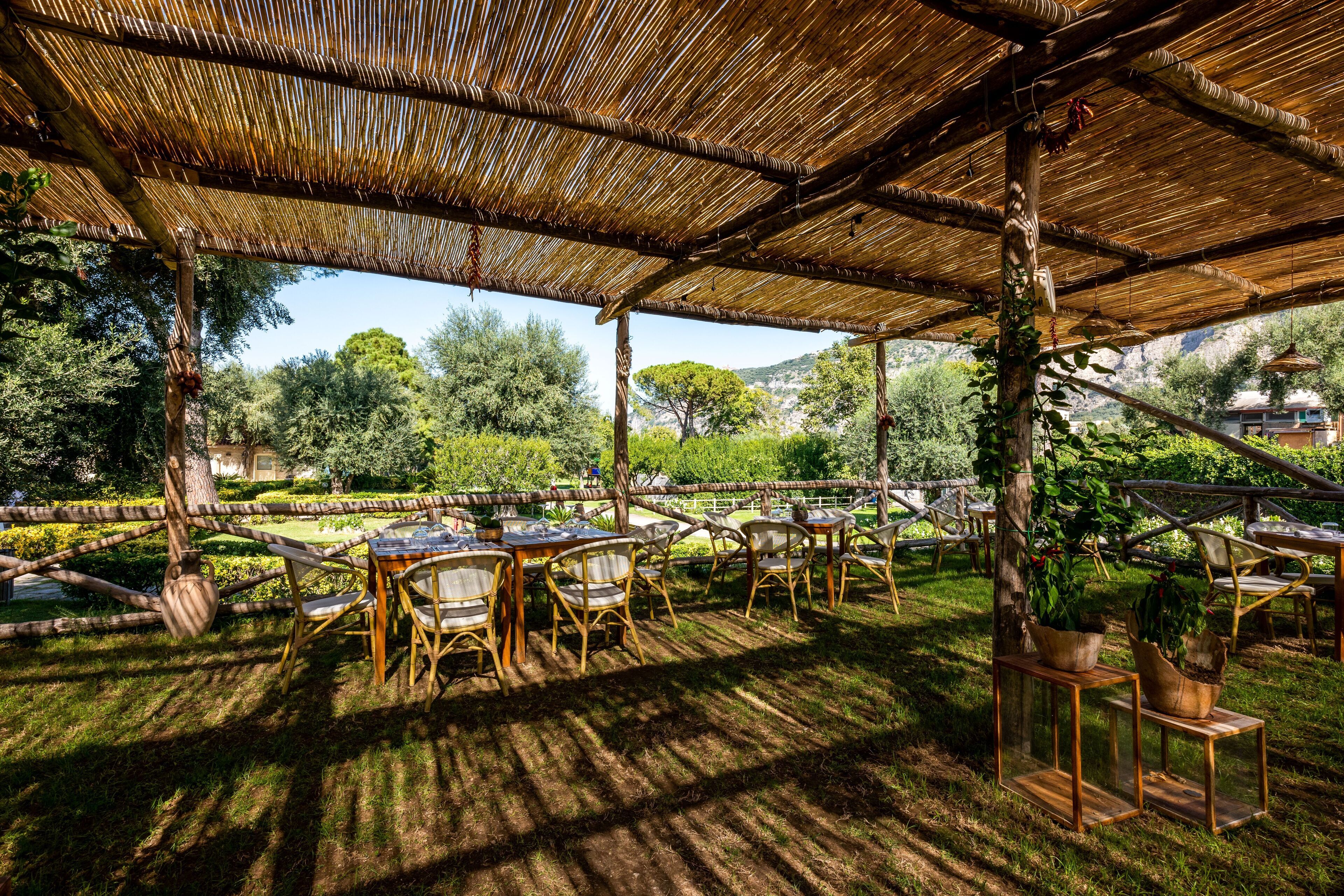 Un espace extérieur aménagé avec des tables et des chaises, abrité par un toit en bambou et entouré de verdure et d’arbres.