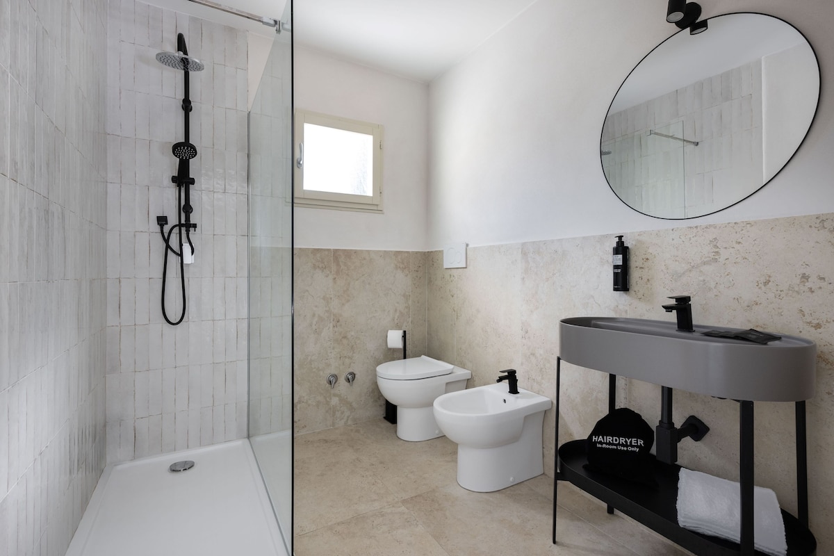 Een moderne badkamer met een douchecabine van glas, een toilet, een bidet en een wastafel met spiegel erboven.
