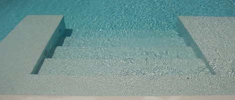 A clear blue pool with steps leading into it, surrounded by white pebbles.