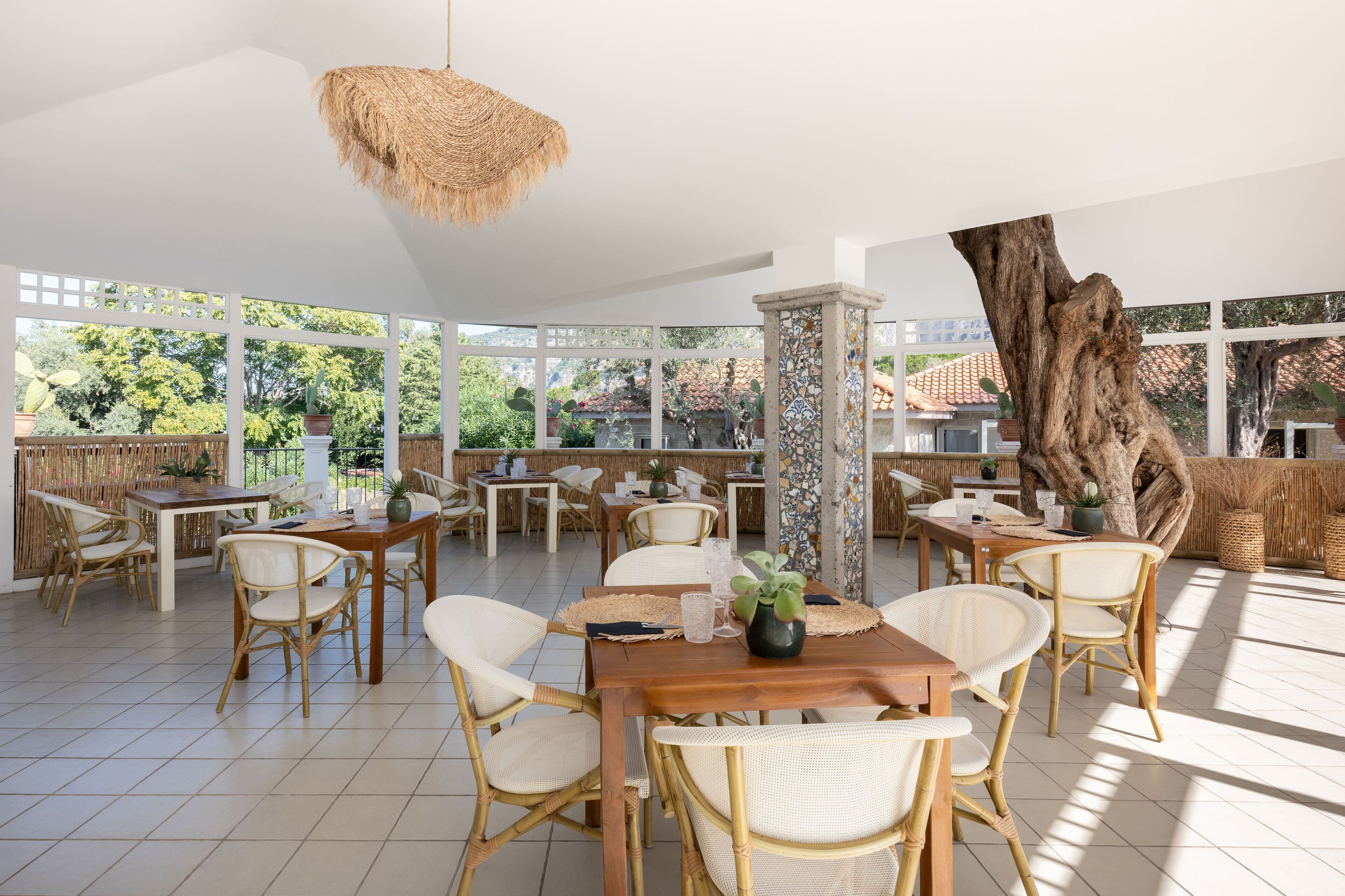 Un amplio espacio de comedor al aire libre con mobiliario de mimbre y un tocón de árbol grande como elemento central.