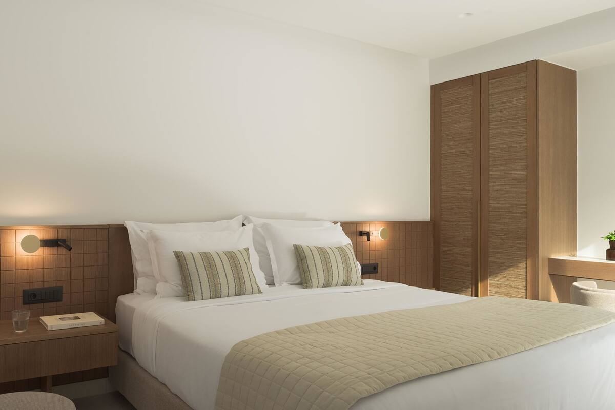 A modern hotel room with a large bed, a bedside table with a lamp, and a nightstand with a book and glass.