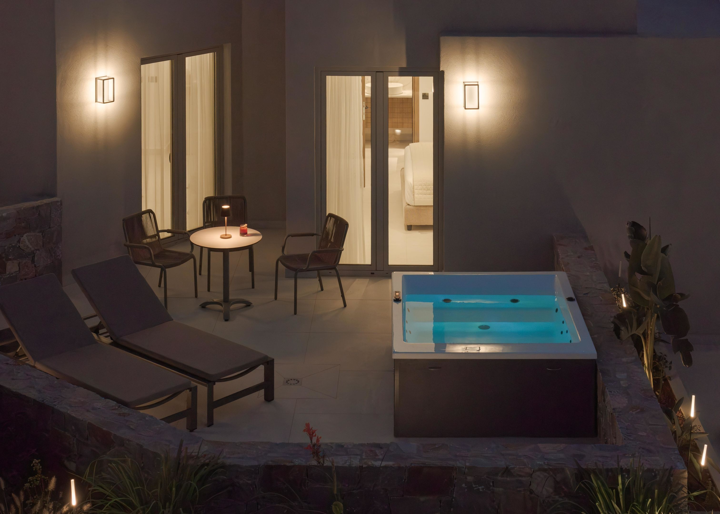 An outdoor patio with a hot tub, lounge chairs, and a table with chairs.