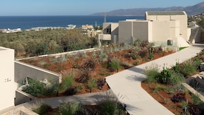 Un edificio moderno con jardín en la azotea, vista despejada al mar y montañas al fondo.
